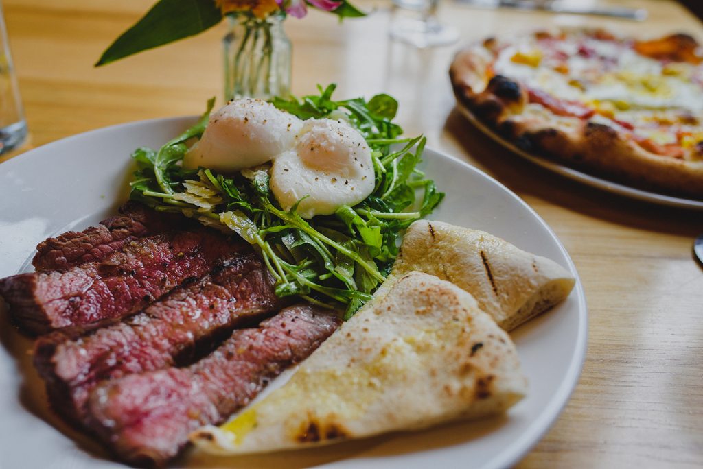 Close up of plate of steak, eggs, greens and pita bread